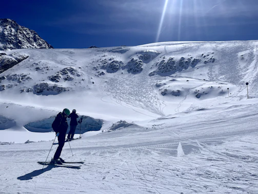 A ski instructor guiding a student down a snowy mountain slope under a clear blue sky.