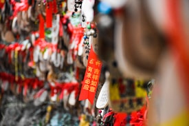 A series of colorful, red and yellow wooden plaques and tags with Chinese characters hang in a dense arrangement, some adorned with beads. The vibrant colors and traditional decorations suggest a cultural or spiritual significance.