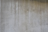 A textured concrete wall with vertical streaks of darker and lighter gray shades, suggesting weathering or staining.