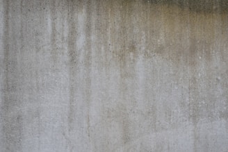 A textured concrete wall with vertical streaks of darker and lighter gray shades, suggesting weathering or staining.