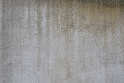 A textured concrete wall with vertical streaks of darker and lighter gray shades, suggesting weathering or staining.