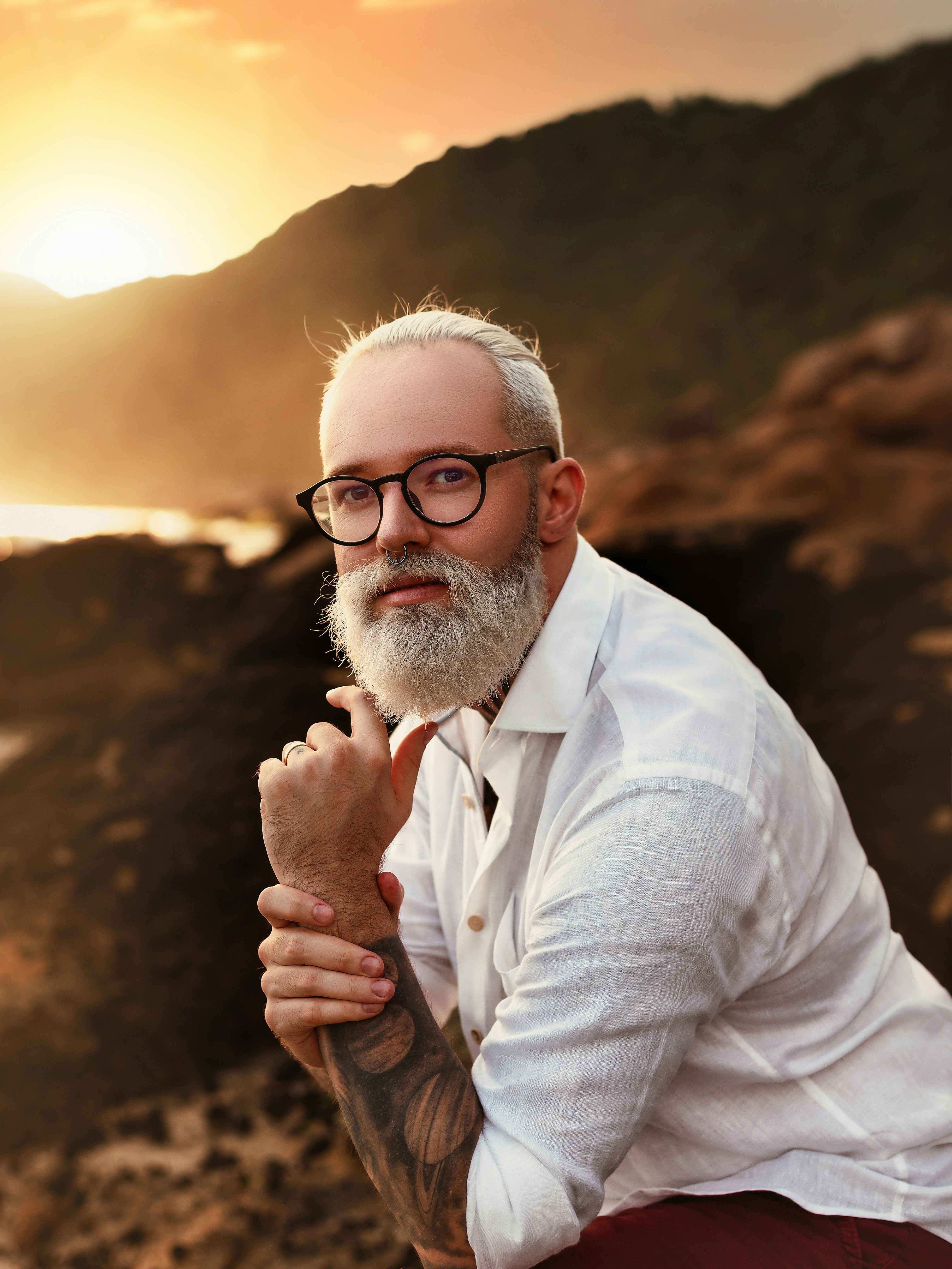a man with a beard and glasses sitting on a rock