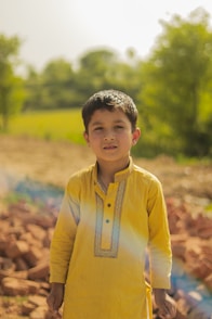 a young boy in a yellow shirt standing in front of a pile of rocks