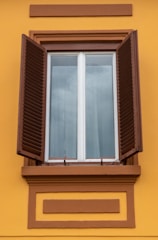 a window with brown shutters on a yellow building