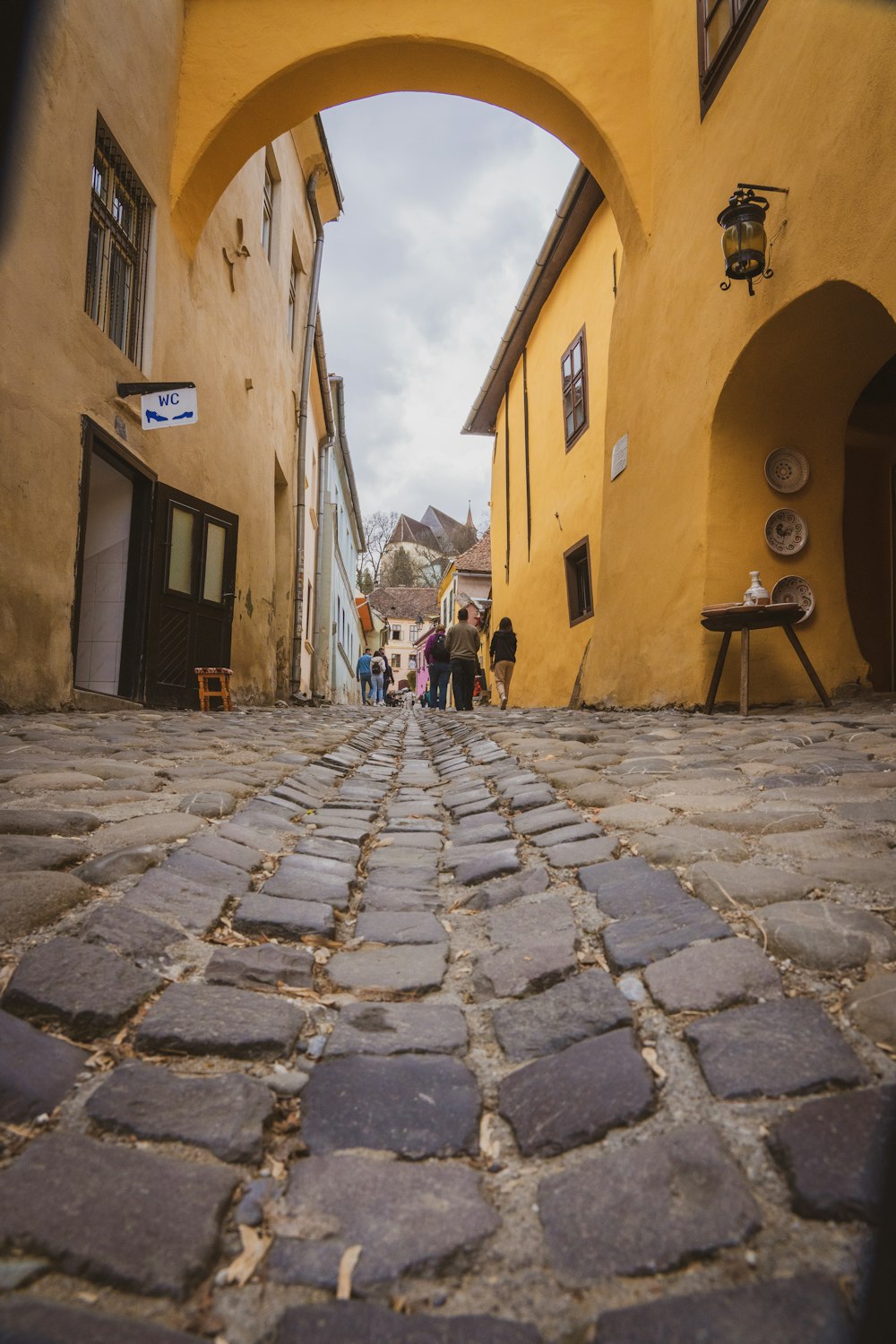 a cobblestone street with people walking under an arch