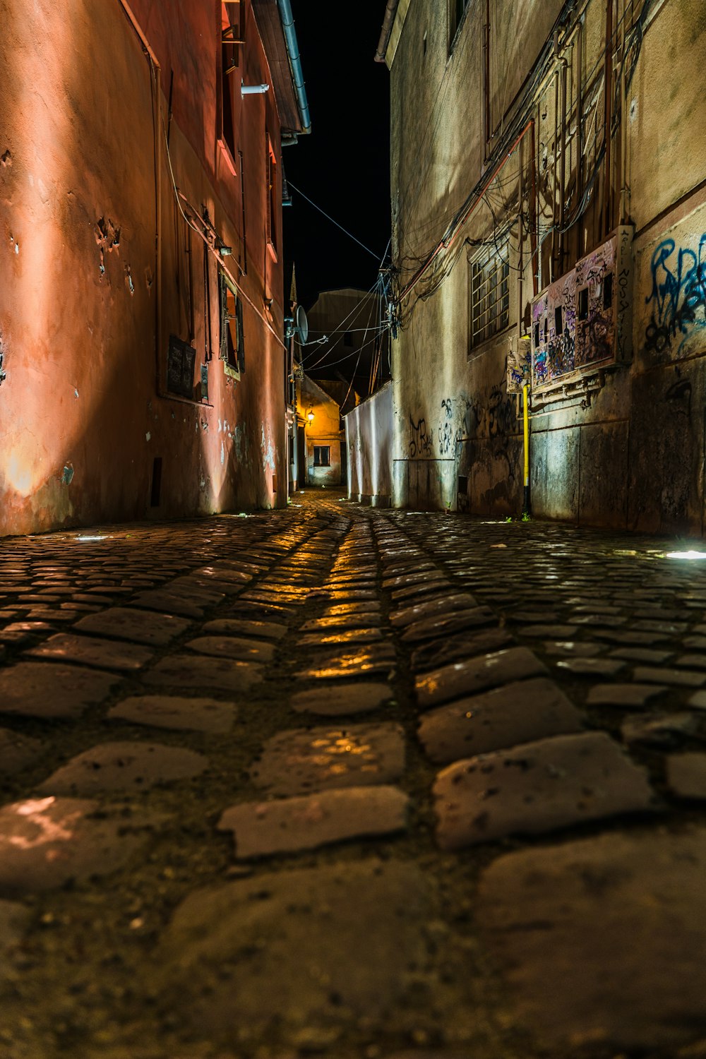 a cobblestone street at night with graffiti on the walls