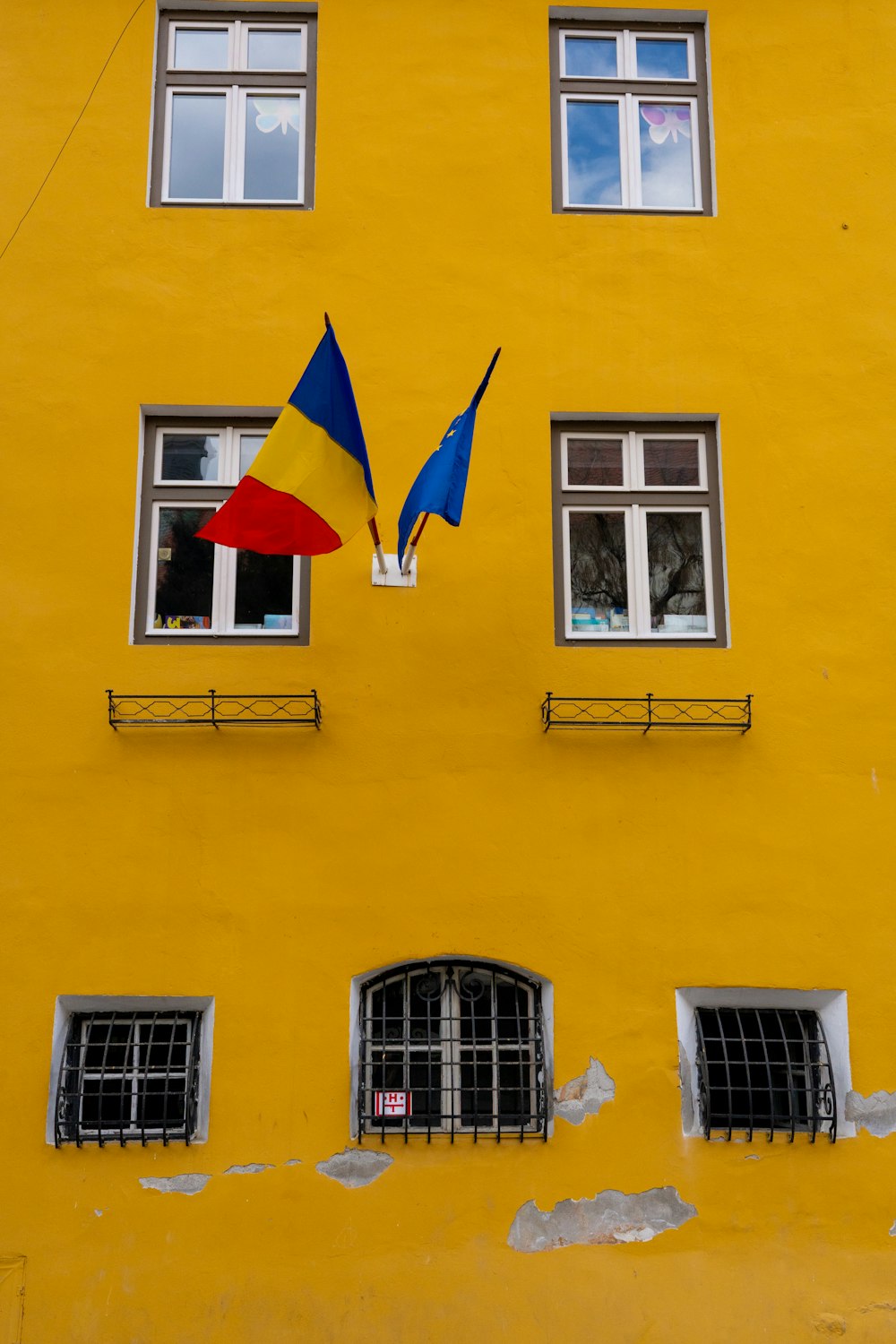 a yellow building with two windows and a red and blue umbrella