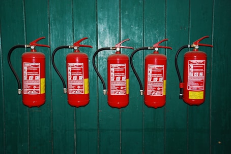 four fire extinguishers lined up against a green wall