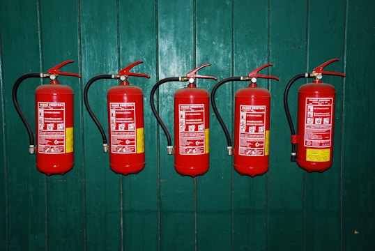 four fire extinguishers lined up against a green wall