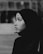Profile view of a woman wearing a hijab, creating a strong contrast between the dark fabric and her facial features. The background is blurred, drawing attention to her contemplative expression.