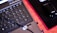 A close-up of a laptop keyboard in the foreground, with a numeric keypad featuring visible keys like 'Enter,' 'Delete,' and number pad digits. To the right, there is a black computer mouse placed on a black mouse pad with red trim. A laptop cable is also visible, crossing over the keyboard.