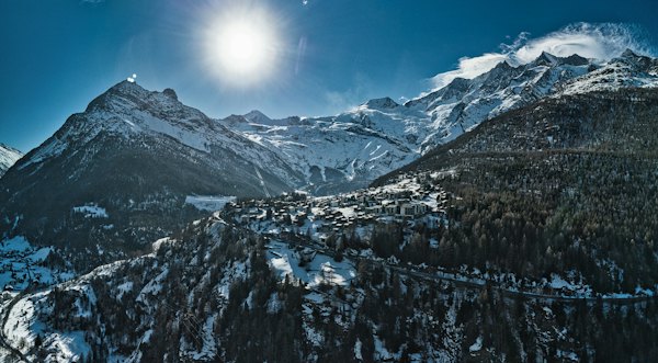 The sun shines brightly over a snowy mountain range — Saas-Fee, Switzerland