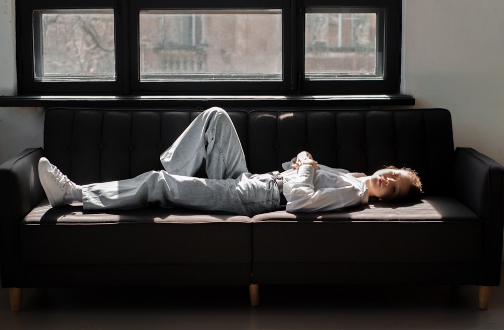 a man laying on top of a couch next to a window