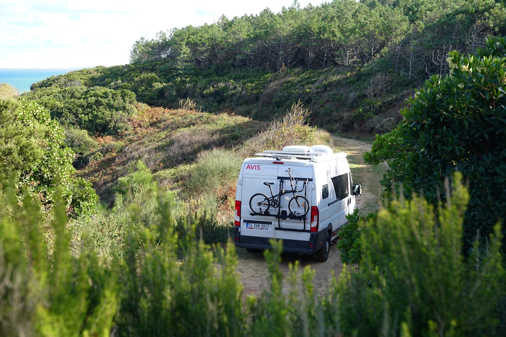 a van parked on a dirt road with a bike mounted to the back of it