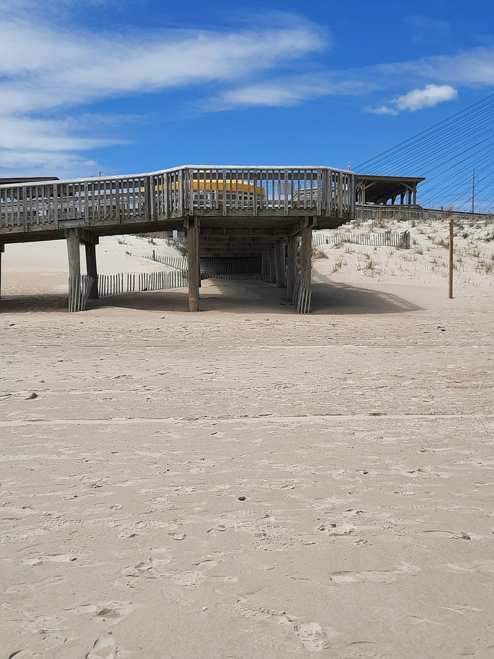 a wooden bridge over a sandy beach under a blue sky
