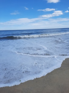 A sunlit sandy beach with gentle waves rolling in under a clear blue sky.