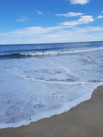 A sunlit sandy beach with gentle waves rolling in under a clear blue sky.