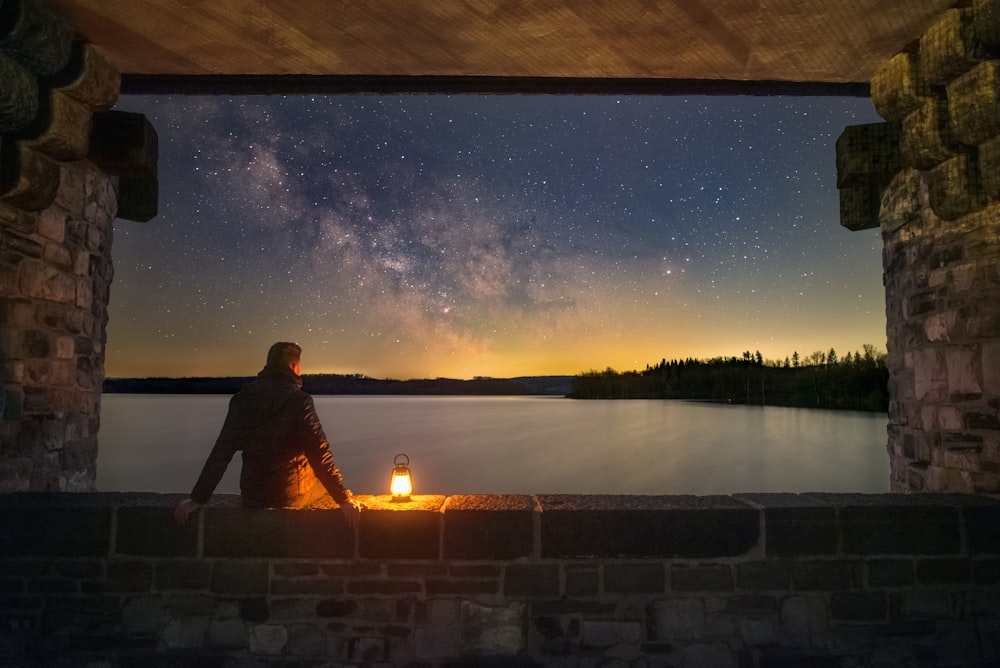 a person sitting on a ledge looking at the night sky