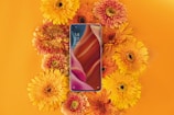 a cell phone surrounded by flowers on an orange background
