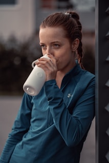 a woman is drinking from a white cup