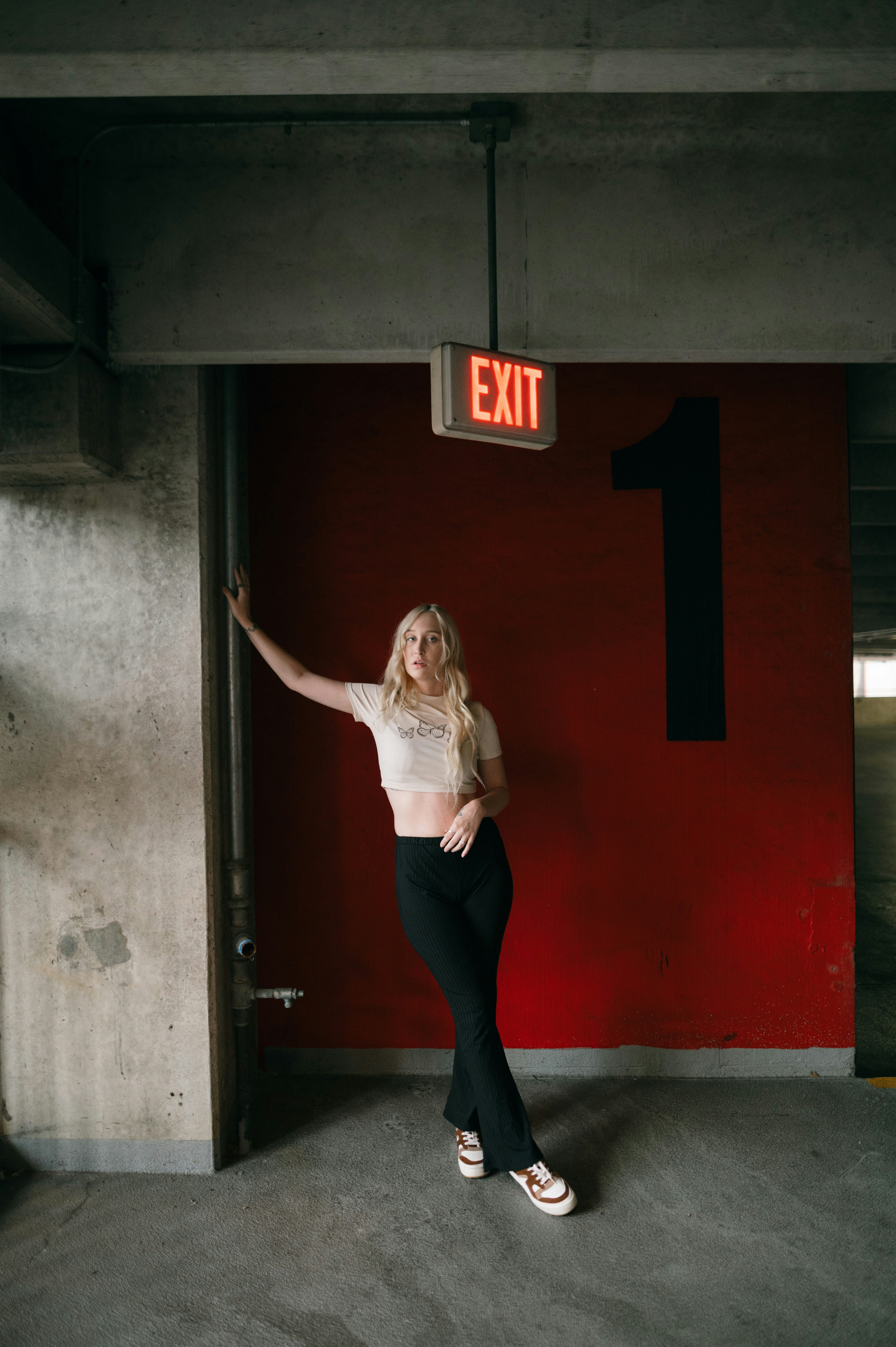 A woman in a white shirt and black pants standing in front of a exit ...