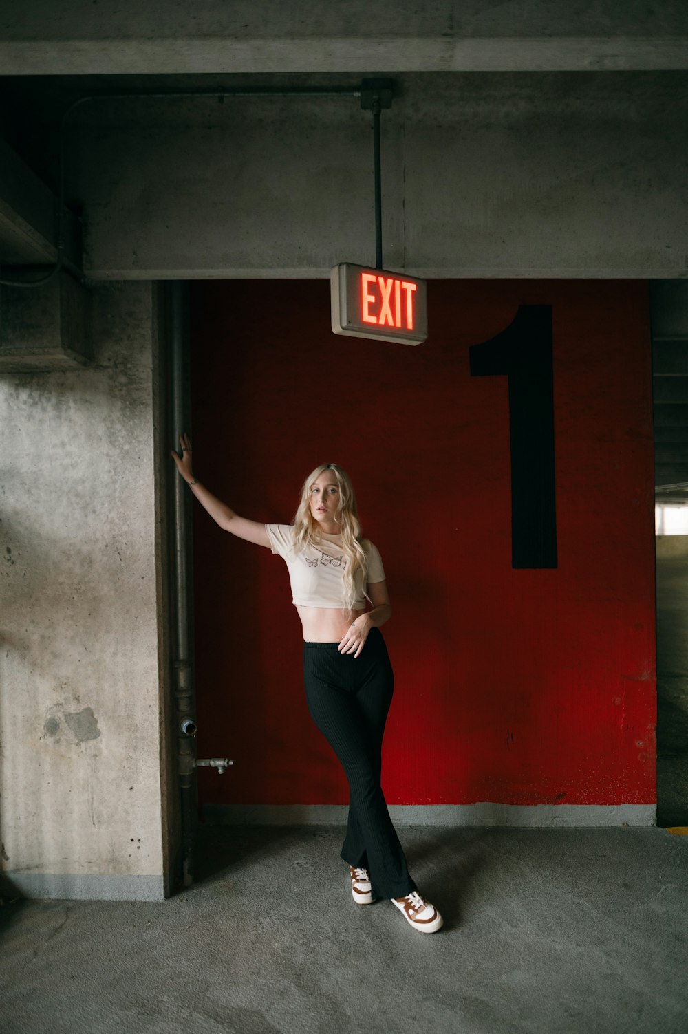 a woman in a white shirt and black pants standing in front of a exit sign