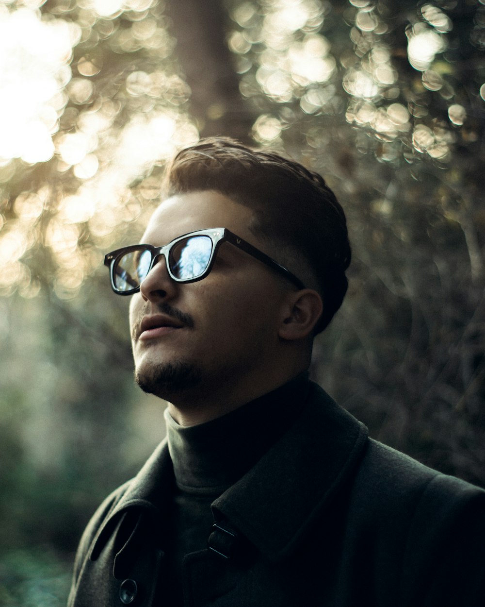 a man wearing sunglasses standing in a forest