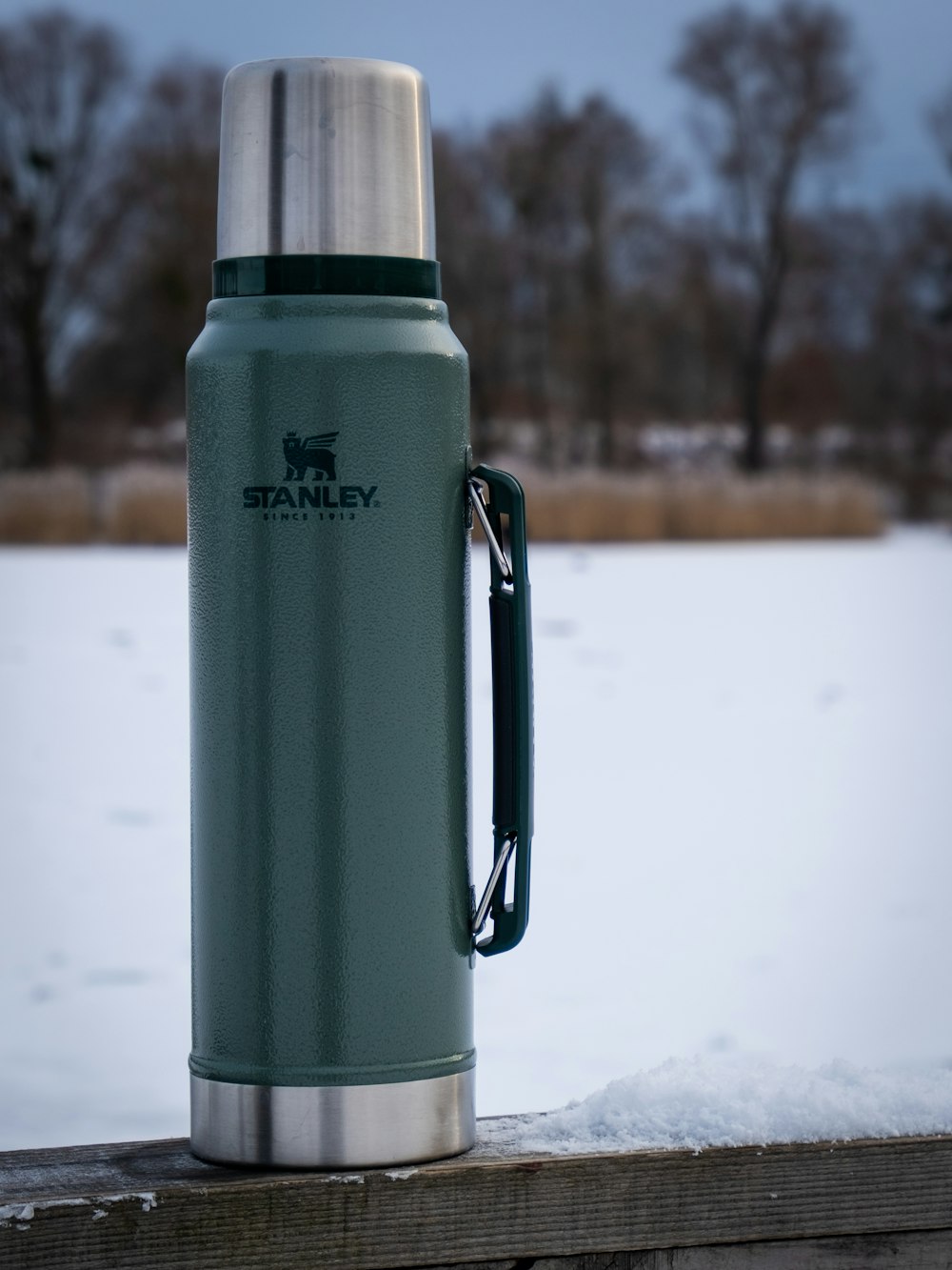 a stainless steel water bottle sitting on top of a wooden fence