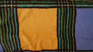 A fabric pattern featuring large blocks of color, including a prominent yellow square and a blue section. The pattern is bordered and intersected by black, green, and turquoise stripes, creating a grid-like design.