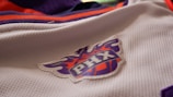 A close-up view of a sports jersey featuring a logo with the letters 'PHX' on a basketball design. The jersey is predominantly white with orange and purple accents.
