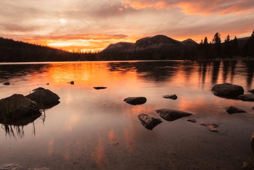 a sunset over a lake with rocks in the foreground