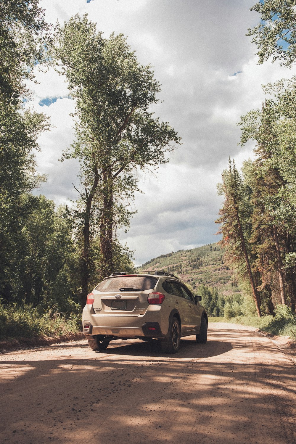 a white car driving down a dirt road next to a forest