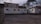 Two mobile trailers are situated in front of a brick building with graffiti. The area is surrounded by leafless trees, and there is a traffic cone and some trash bins next to the trailers. The ground is paved, and the scene has a somewhat neglected, industrial feel.