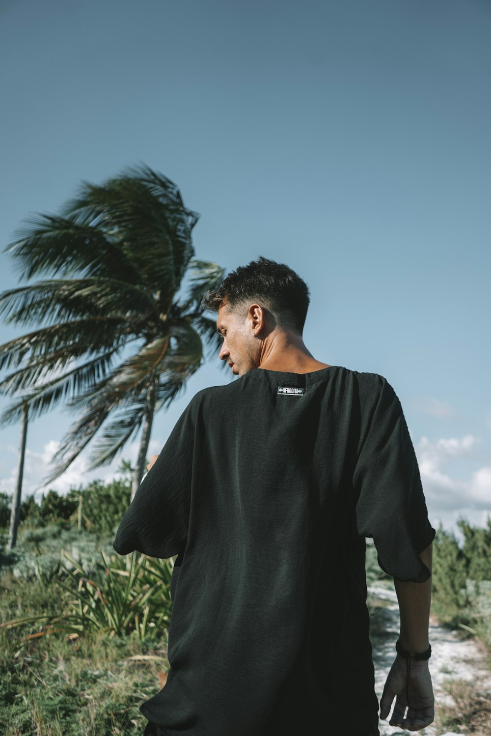 a man walking down a dirt road next to a palm tree