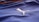 A close-up of a textured blue fabric with a white embroidered logo of a leaping animal, likely representing a brand. The fabric appears to be part of a sports jersey, with fine linear stitching visible.