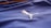 A close-up of a textured blue fabric with a white embroidered logo of a leaping animal, likely representing a brand. The fabric appears to be part of a sports jersey, with fine linear stitching visible.