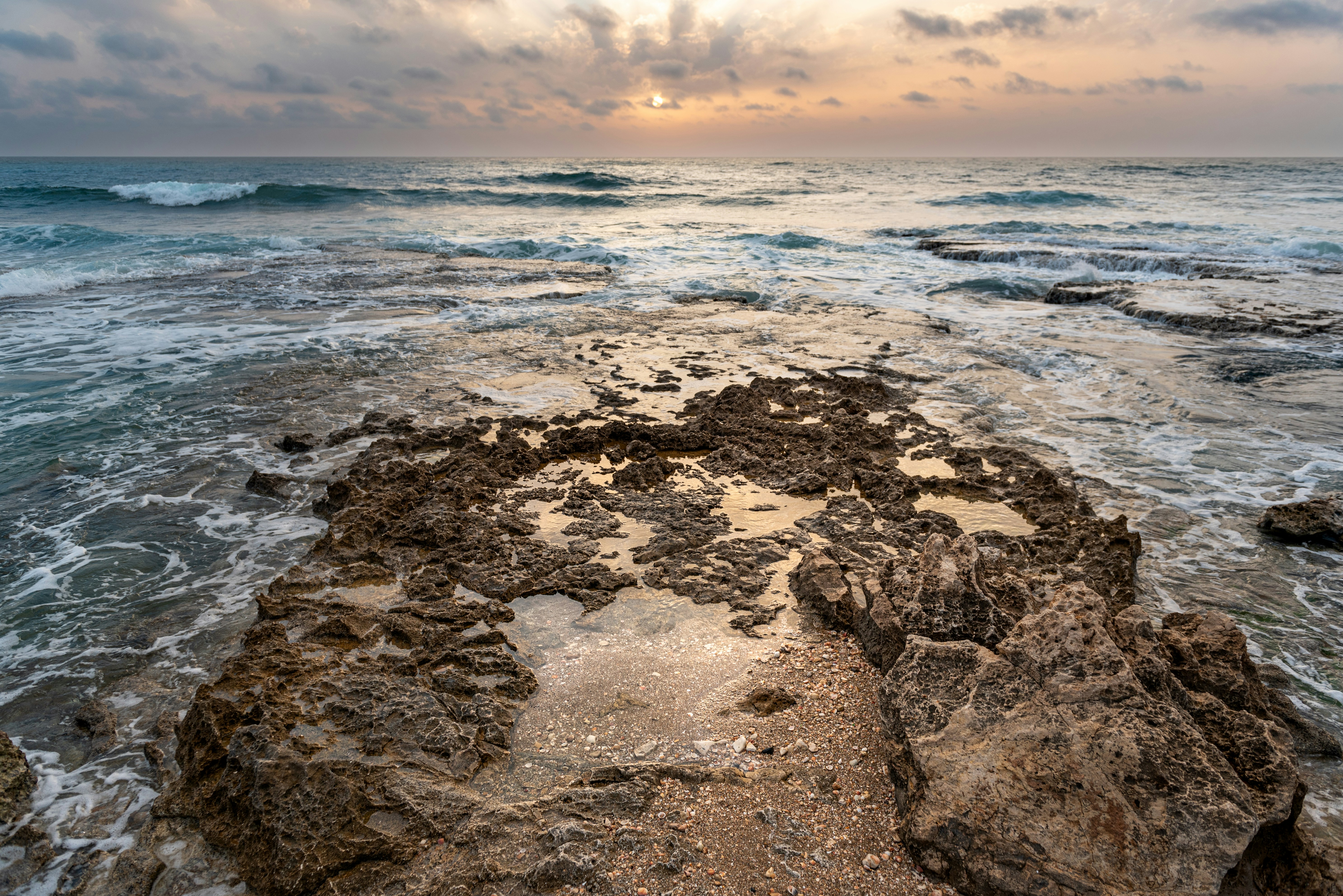 the sun is setting over the ocean on a rocky shore