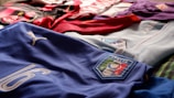 Various football (soccer) jerseys laid out on a surface. The prominently featured jersey in the foreground is blue with the word 'Italia,' a Puma logo, and the number 16. Other jerseys in the background include red, black, white, and purple colors.