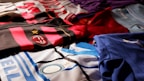 A collection of colorful soccer jerseys is laid out, each featuring distinctive team logos and color patterns. The jerseys include stripes, stars, and various shades, providing a rich visual contrast.