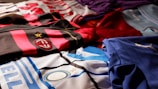 A collection of colorful soccer jerseys is laid out, each featuring distinctive team logos and color patterns. The jerseys include stripes, stars, and various shades, providing a rich visual contrast.