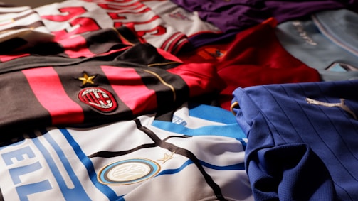 A collection of colorful soccer jerseys is laid out, each featuring distinctive team logos and color patterns. The jerseys include stripes, stars, and various shades, providing a rich visual contrast.
