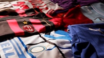 A collection of colorful soccer jerseys is laid out, each featuring distinctive team logos and color patterns. The jerseys include stripes, stars, and various shades, providing a rich visual contrast.