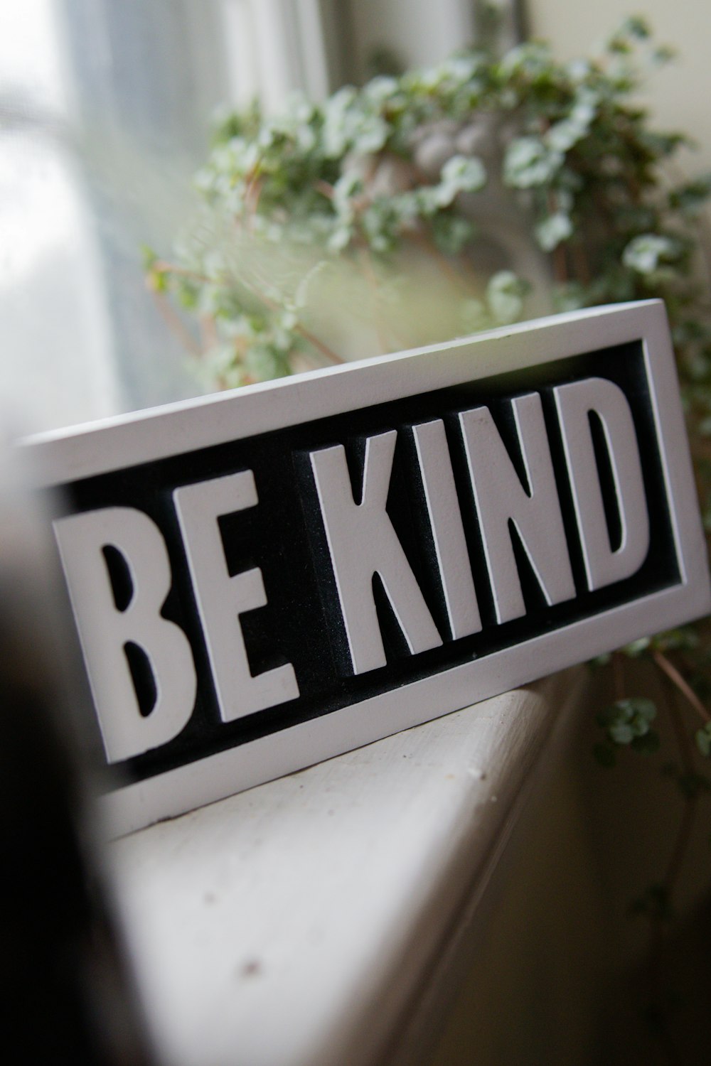 a black and white be kind sign sitting on a window sill