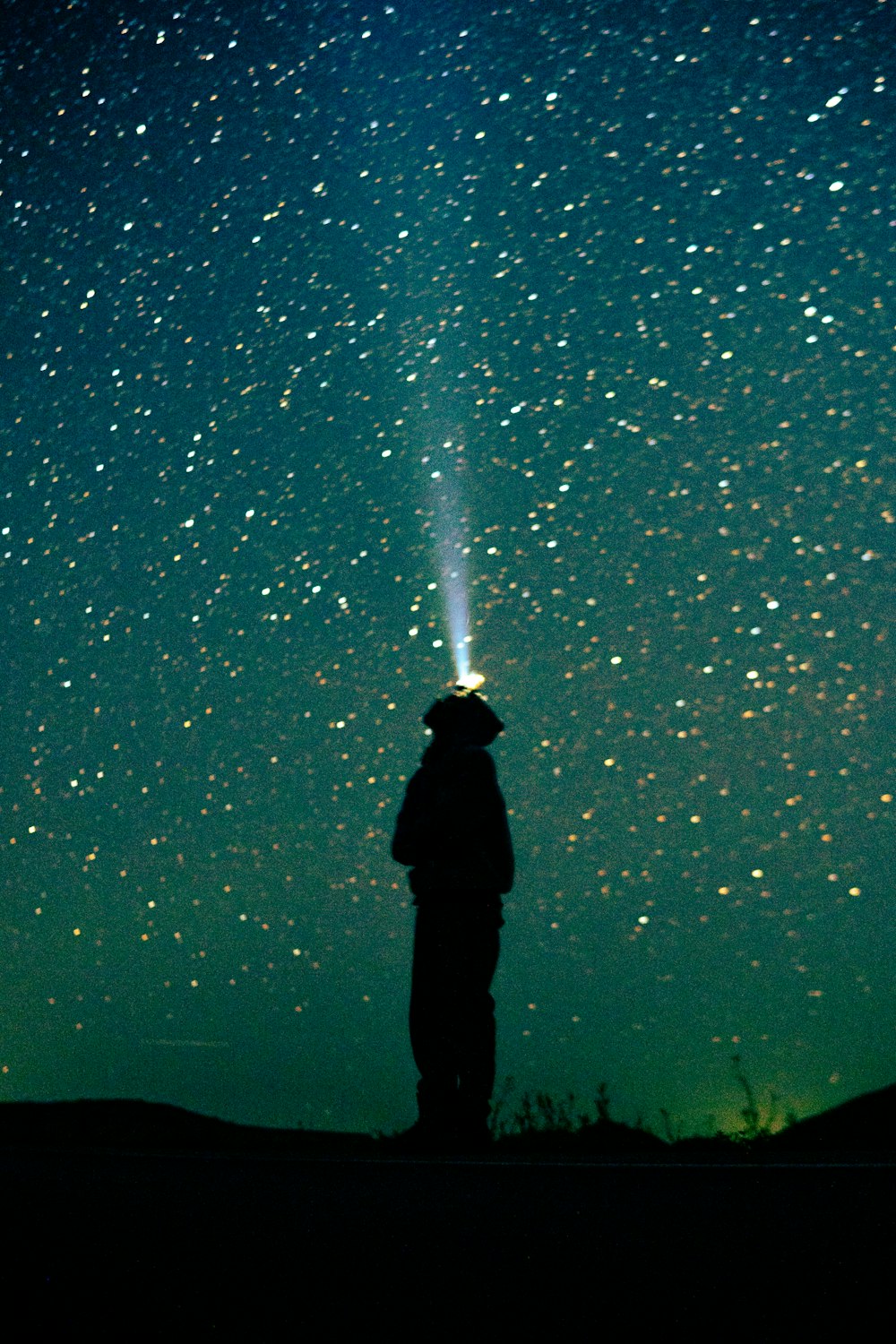 a man standing on top of a hill under a sky filled with stars