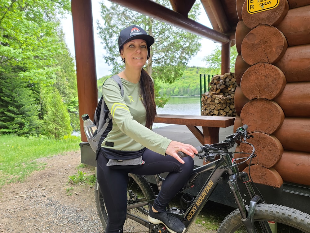 a woman sitting on top of a bike next to a log cabin