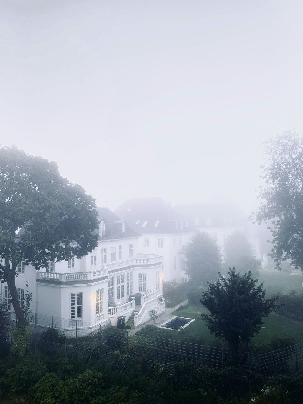 a large white house surrounded by trees on a foggy day