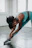 A smiling woman stretching on a Pilates reformer in a cozy, sunlit studio.