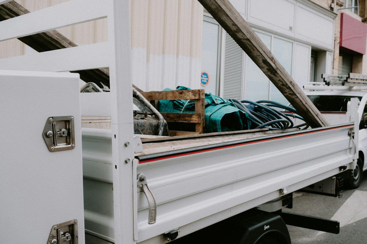 The cargo bed and drop sides of a white small truck, loaded with a wooden crate and a coiled hose