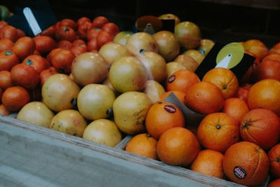 A variety of fruits are arranged in a market display. The image features a selection of oranges and grapefruits placed neatly in wooden crates. Some of the fruits have stickers on them, indicating they are for sale. The overall composition is orderly and colorful, with the different shades of orange and yellow creating a warm visual appeal.