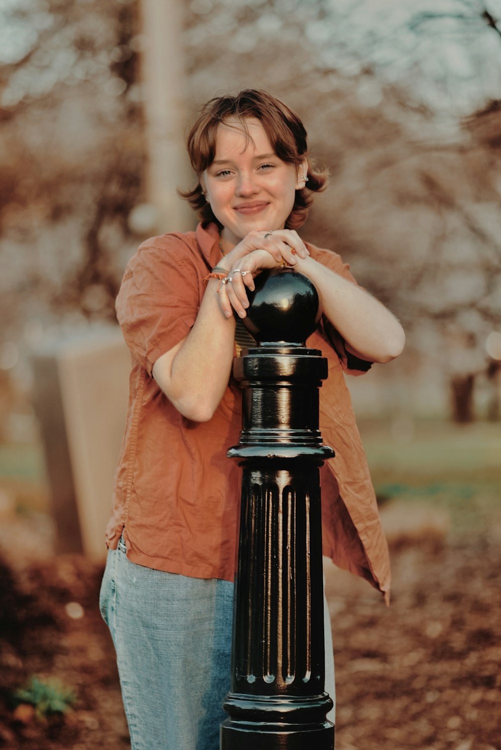a woman leaning on a black post in a park